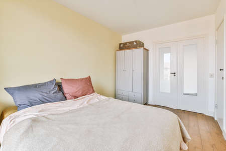 Home interior design of bedroom with bed and wooden wardrobe placed in corner near window in modern...