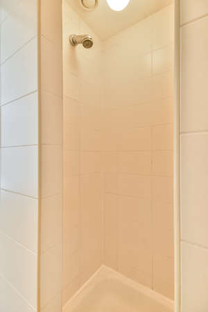 Wall hung toilet and small sink in corner in lavatory room with beige tile and shower cabinの写真素材