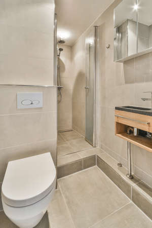 Flush toilet located between sink and shower in small tiled bathroom of contemporary apartment
