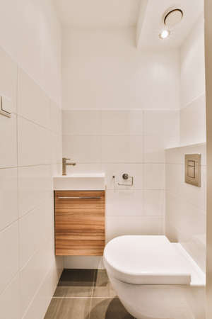 Interior of narrow restroom with sink and wall hung toilet with white walls and checkered floor