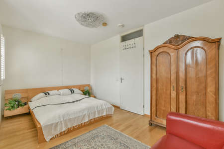 Comfortable bed with ornamental blanket placed near glass door and wardrobe with mirror in light...