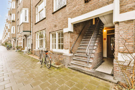 The front view of a brick building with signs, pavement and wooden doors lead to the apartment