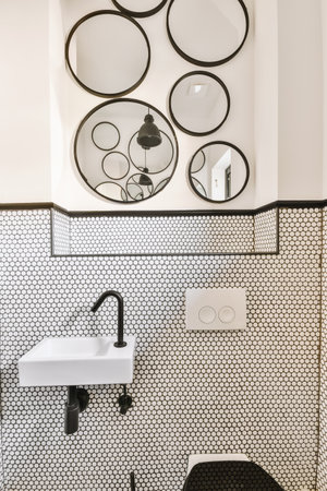Modern flush toilet and ceramic sink installed on white tiled walls near mirror and towel in small...