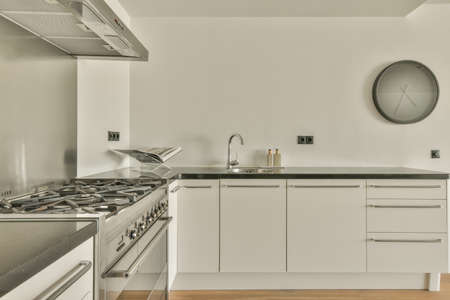Fragment of interior of light narrow home kitchen with minimalist style white furniture with sink and stoveの写真素材