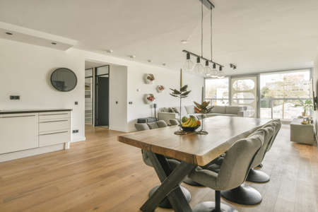 Contemporary minimalist style interior design of light studio apartment with wooden table and chairs in dining zone between open kitchen and living room with white walls and parquet floorの写真素材