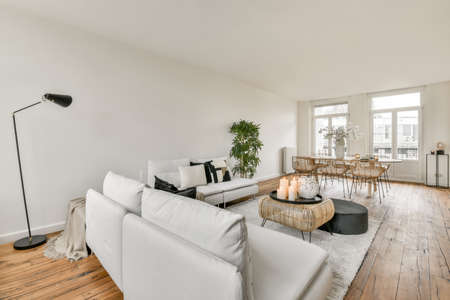 Shabby wooden table with chairs and vase located near comfortable couch against light walls with...