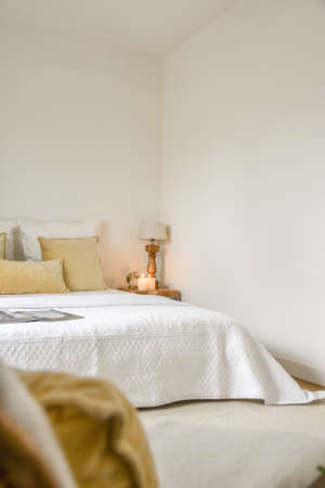 Sunlit bed covered with blanket in light contemporary bedroom with shelves and decorationsの写真素材