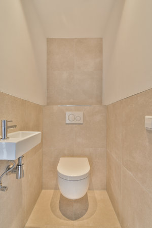 Wall hung toilet and small sink in corner in lavatory room with beige tile