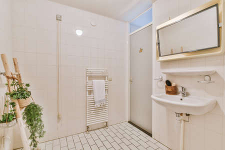 Cupboard with sink and mirror attached to tiled wall near door and drying rack in modern restroomの写真素材