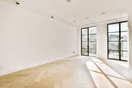 Interior of empty white room with large balcony windows and wooden parquet floor