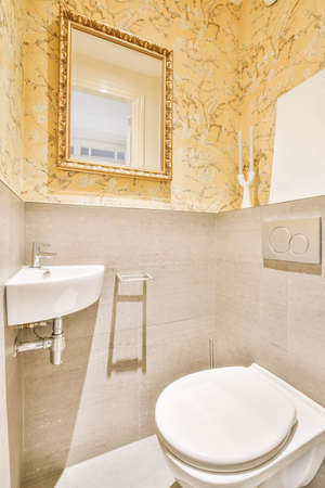 Modern flush toilet and ceramic sink installed on white tiled walls near mirror and towel in small...
