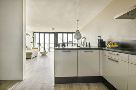 Open plan black kitchen in white living room with dining table and gray sofaの写真素材