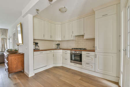 Modern minimalist style interior design of studio apartment with open white kitchen and dining zone with table and chairs illuminated by loft style lampの写真素材
