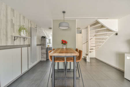 Shabby wooden table with chairs and vase located near comfortable couch against light walls with...