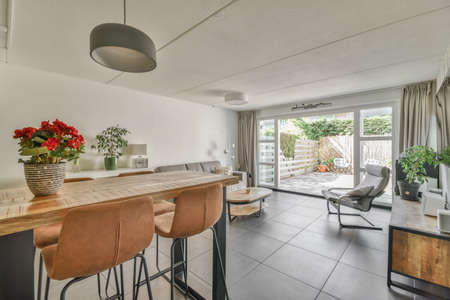 Shabby wooden table with chairs and vase located near comfortable couch against light walls with decorations and TV in modern apartmentの写真素材