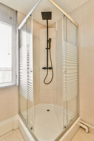 Shower faucets attached to tiled wall near glass partition and ornamental curtail in washroom at...