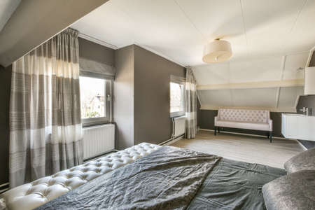 Comfortable bed placed near green wall in modern minimalist style mansard bedroom with windows