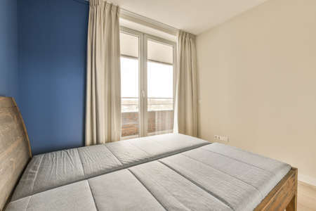 Sunlit bed covered with blanket in light contemporary bedroom with shelves and decorations
