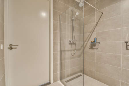 Bathroom with white tiled walls and open shower near sink base cabinet in lightの写真素材