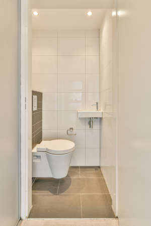 Interior of narrow restroom with sink and wall hung toilet with white walls and checkered floor
