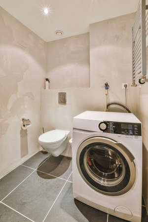 Interior of narrow restroom with washing machine and wall hung toilet with white walls and checkered floorの写真素材