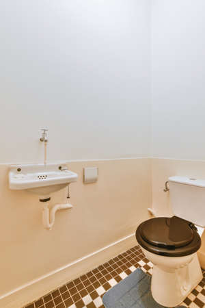 Interior of narrow restroom with sink and wall hung toilet with white walls and checkered floor