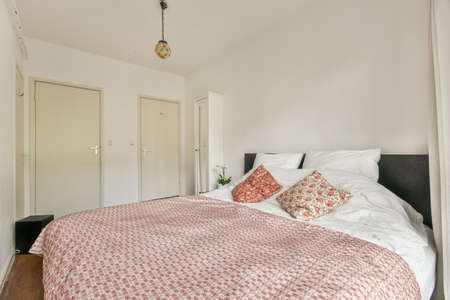 Comfortable bed covered with checkered blanket and located in light bedroom of modern apartment