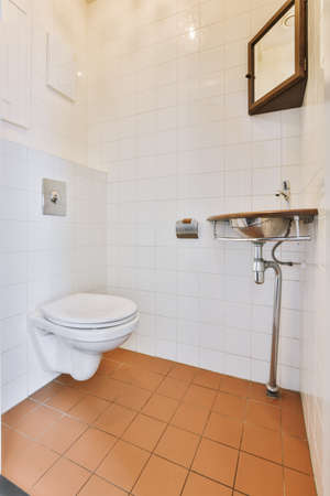 Interior of narrow restroom with sink and wall hung toilet with white walls and checkered floor