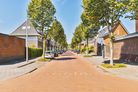 Panorama view of brick houses from an empty sidewalk street with cars, trees and lanternsの写真素材