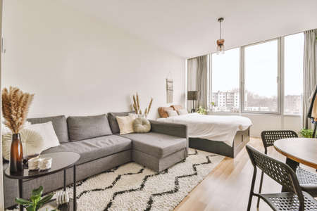 Table with chairs and flowers located near lounge area and kitchen in spacious room of contemporary apartmentの写真素材
