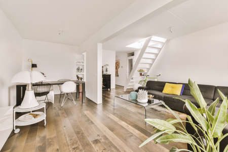 Shabby wooden table with chairs and vase located near comfortable couch against light walls with...