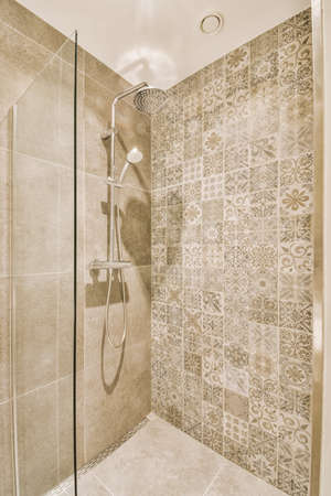 Shower faucets attached to tiled wall near glass partition and ornamental curtail in washroom at homeの写真素材