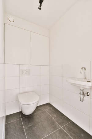 Interior of narrow restroom with sink and wall hung toilet with white walls and checkered floorの写真素材