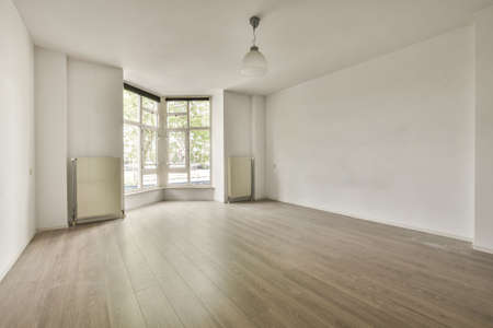 Interior of empty white room with large balcony windows with curtains and wooden parquet floor