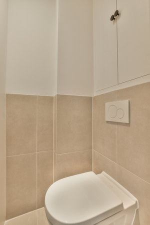 Interior of narrow restroom with sink and wall hung toilet with white walls and checkered floor