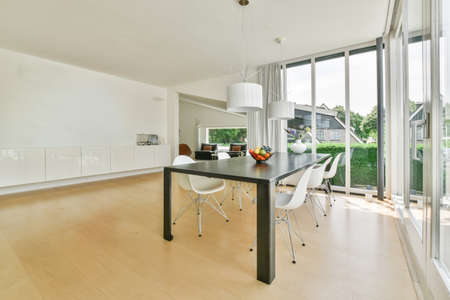 Wooden table with vase and chairs placed near opened balcony door in light dining room at home