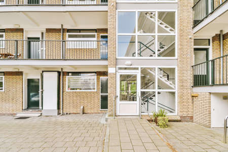 The front view of a brick building with signs,pavement and wooden doors lead to the apartment
