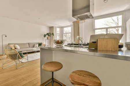 Table with chairs and flowers located near lounge area and kitchen in spacious room of contemporary...