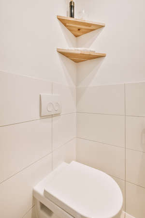 Interior of narrow restroom with wall hung toilet with white walls and checkered floor