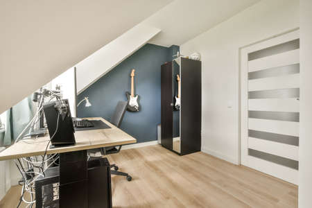 Comfortable chair placed near desk with computer monitors and whiteboard in light workplace in...