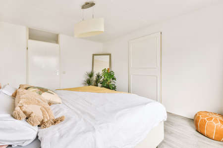 Home interior design of bedroom with bed and wooden wardrobe placed in corner near window in modern...