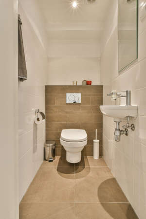 Interior of narrow restroom with sink and wall hung toilet with white walls and checkered floor