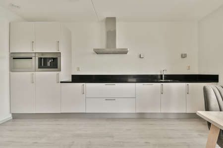 Table with chairs and flowers located near lounge area and kitchen in spacious room of contemporary...