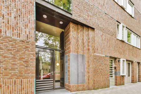 The front view of a brick building with signs,pavement and wooden doors lead to the apartment
