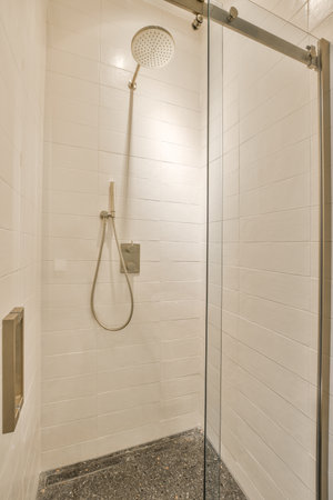 Shower faucets attached to tiled wall near glass partition and ornamental curtail in washroom at...