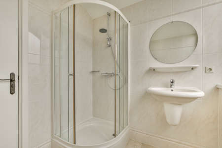 Sinks with mirrors and clean bathtub located near shower box with glass door in modern bathroom with white tiled wallsの写真素材