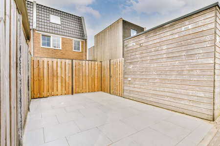Neat paved patio with sitting area and small garden near wooden fence