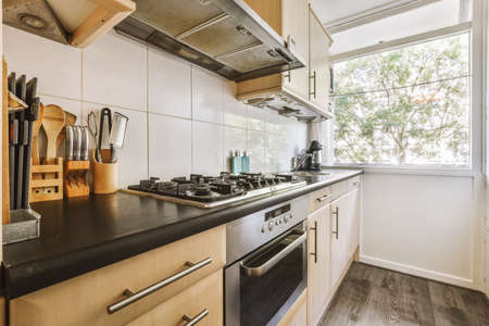 Fragment of interior of light narrow home kitchen with minimalist style white furniture with sink...