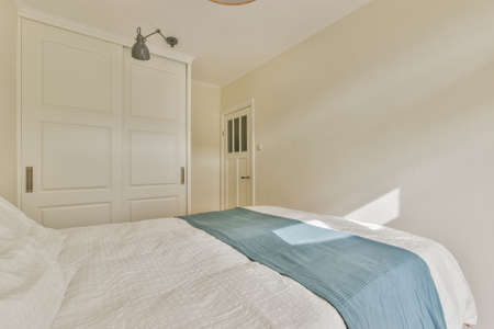 Comfortable bed covered with checkered blanket and located in light bedroom of modern apartment