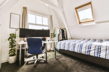 Comfortable chair placed near table with computer monitors against blank whiteboard and mirror in light home office in contemporary flatの写真素材